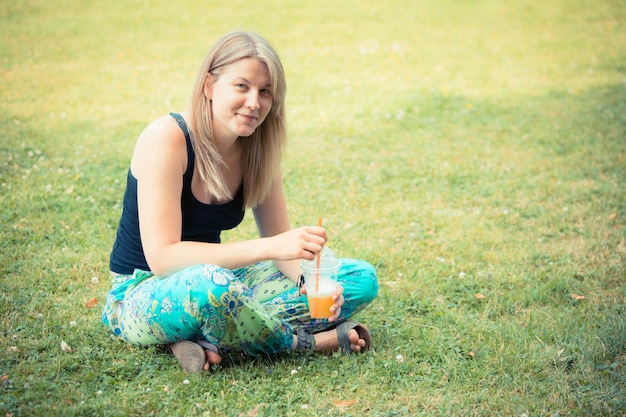 Donna bionda che beve succo di frutta al parco