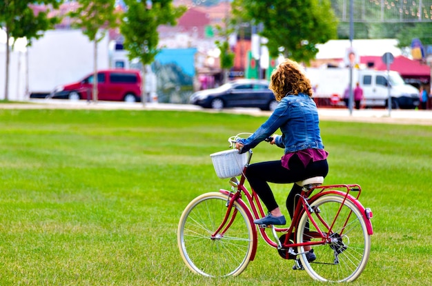 Donna bionda che cammina nel parco con un denim blu su una bicicletta rossa.