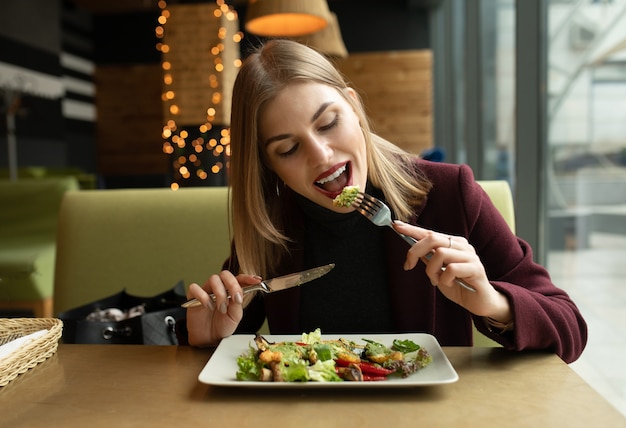 Donna bionda che mangia insalata di eco gustosa sana verde sul caffè della città