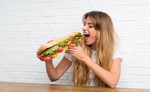 Donna bionda che mangia un panino gigante