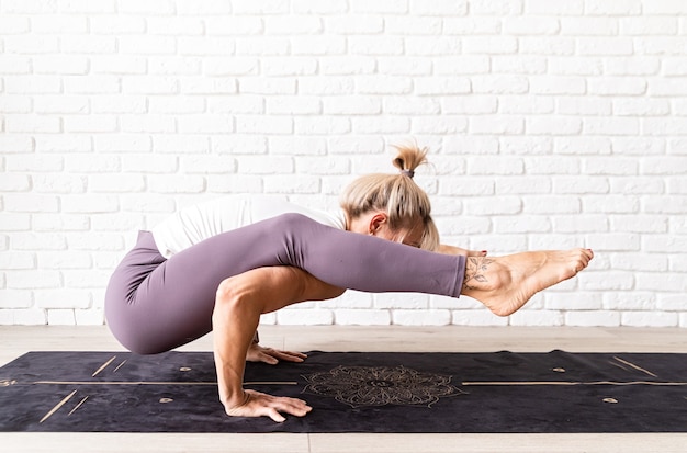 Donna bionda che pratica yoga a casa facendo esercizi sul tappetino