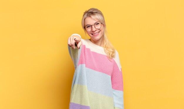 Donna bionda che punta alla telecamera con un sorriso soddisfatto, fiducioso, amichevole, scegliendo te