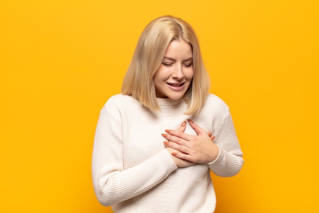 Donna bionda che sembra triste, ferita e affranta, tenendo entrambe le mani vicino al cuore, piangendo e sentendosi depressa