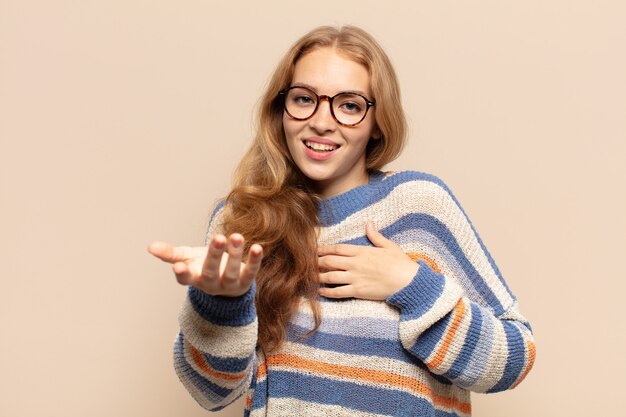 Donna bionda che si sente felice e innamorata, sorride con una mano vicino al cuore e l'altra tesa davanti