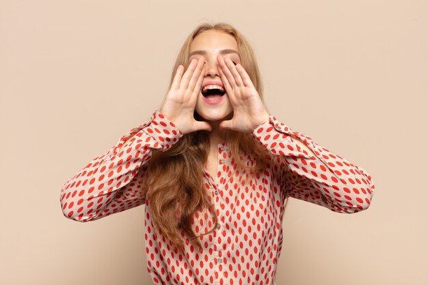 Donna bionda che si sente felice, eccitata e positiva, che grida con le mani vicino alla bocca, chiamando