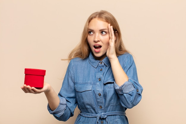 Donna bionda che si sente felice, eccitata e sorpresa, guardando di lato con entrambe le mani sul viso