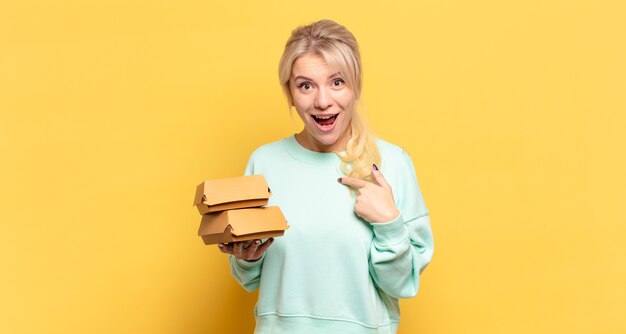 Donna bionda che si sente felice, sorpresa e orgogliosa, indicando se stessa con uno sguardo eccitato e stupito