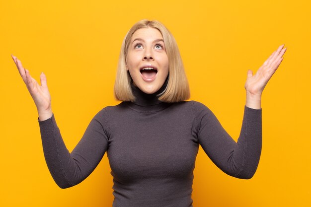 Donna bionda che si sente felice, stupita, fortunata e sorpresa, celebrando la vittoria con entrambe le mani in aria