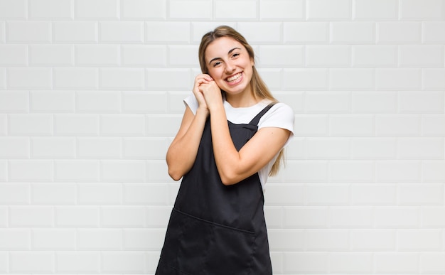 Donna bionda che si sente innamorata e sembra carina, adorabile e felice, sorridendo romanticamente con le mani accanto al viso