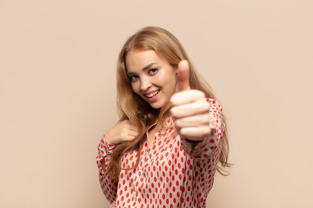 Donna bionda che si sente orgogliosa, spensierata, sicura e felice, sorridendo positivamente con i pollici in su