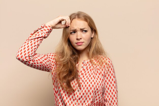 Donna bionda che si sente perplessa e confusa, grattandosi la testa e guardando di lato