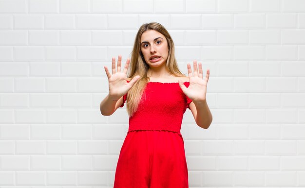 Donna bionda che si sente stupefatta e spaventata, temendo qualcosa di spaventoso, con le mani aperte davanti dicendo di stare lontano