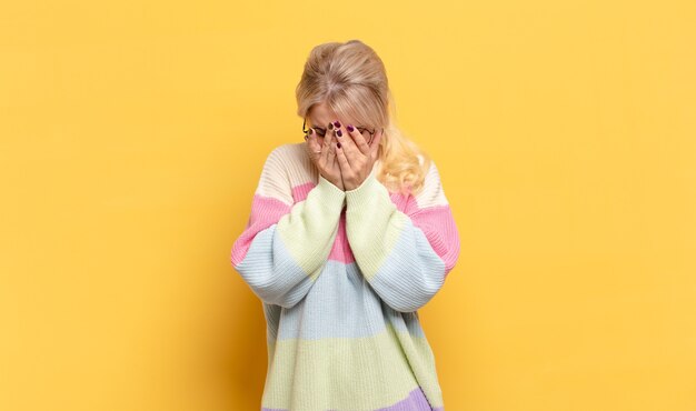 Donna bionda che si sente triste, frustrata, nervosa e depressa, che copre il viso con entrambe le mani, piangendo