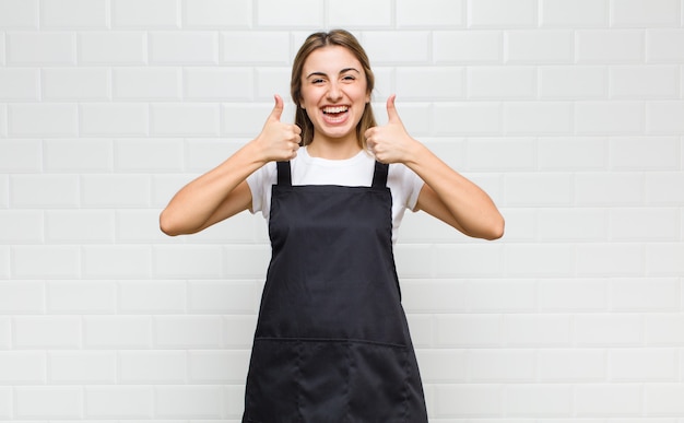 Donna bionda che sorride ampiamente felice, positiva, sicura e di successo, con entrambi i pollici in su