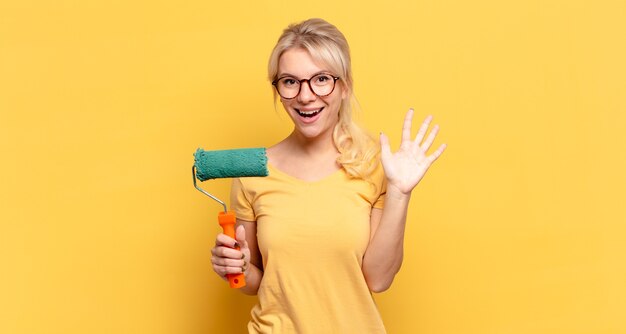 Donna bionda che sorride e sembra amichevole, mostrando il numero cinque o quinto con la mano in avanti, contando alla rovescia