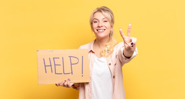 Donna bionda che sorride e sembra felice, spensierata e positiva, gesticolando vittoria o pace con una mano