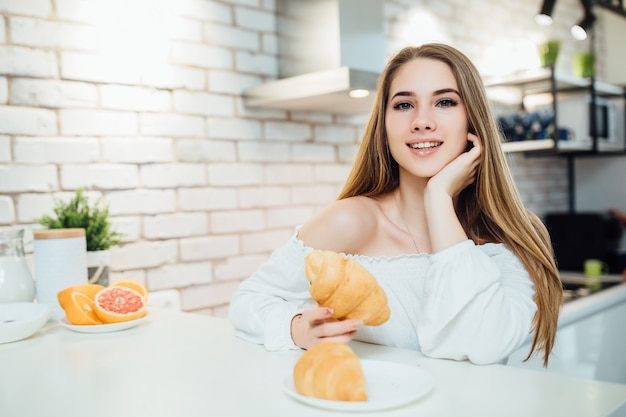 Donna bionda che tiene un croissant e sorride cibo sano mentre è seduto su una sedia.