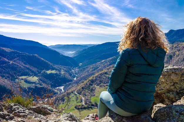 Donna bionda con capelli ricci, seduta su una panchina, guardando le montagne di Ribes, Girona.