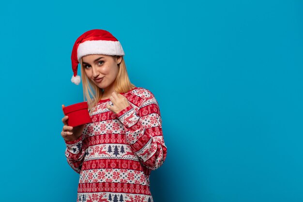 Donna bionda con cappello da Babbo Natale che sembra arrogante, di successo, positiva e orgogliosa, indicando se stessa