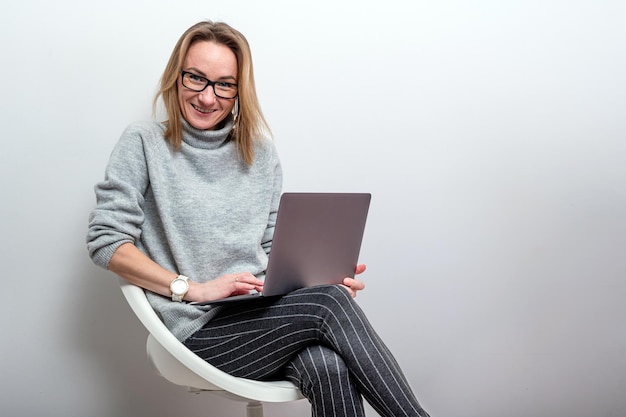 Donna bionda con gli occhiali che lavorano sul concetto di telelavoro del computer isolato su grigio