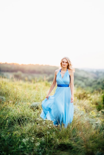 Donna bionda con i capelli sciolti in un vestito azzurro e un ragazzo alla luce del tramonto in natura