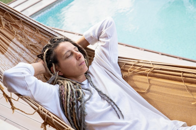 Donna bionda con i dreadlocks che si rilassano con gli occhi chiusi in un'amaca tessuta.