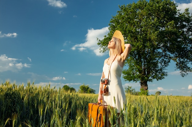 Donna bionda con la valigia e la macchina fotografica nel campo di frumento nell'ora legale