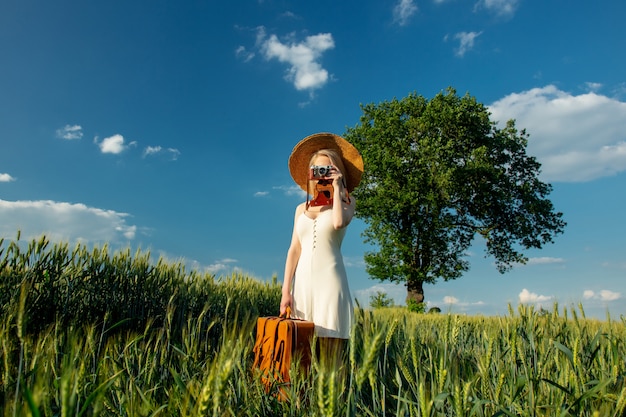 Donna bionda con la valigia e la macchina fotografica nel campo di frumento nell'ora legale