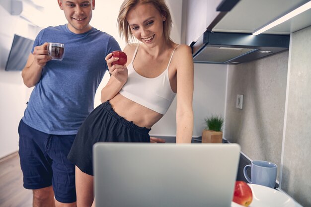 donna bionda con mela che guarda nel computer mentre l'uomo dietro di lei beve il tè