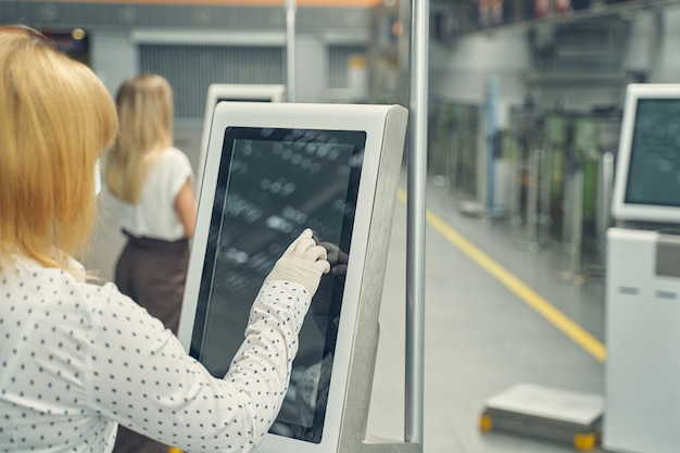 Donna bionda concentrata in piedi e utilizzando il monitor delle informazioni prima dell'imbarco