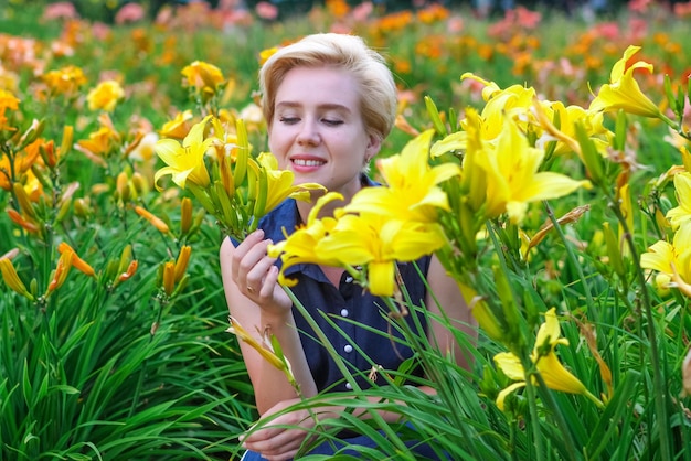 Donna bionda dagli occhi azzurri tra gigli gialli in fiore nel giardino