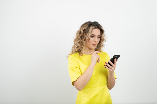 donna bionda dai capelli ricci in abito giallo, controllando il suo cellulare.