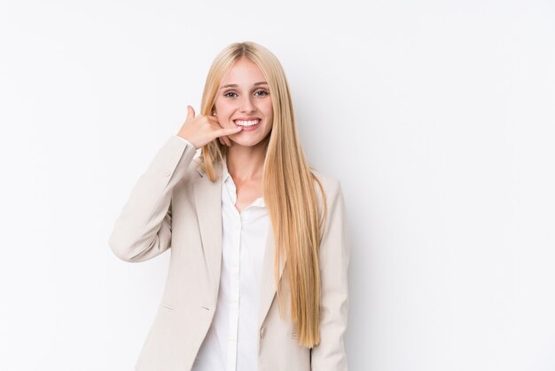 Donna bionda di giovani affari sulla parete bianca che mostra un gesto di chiamata del telefono cellulare con le dita.