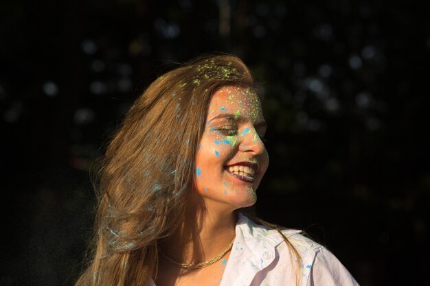 Donna bionda felice in camicia bianca che celebra il festival di Holi nel parco