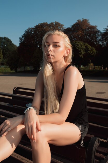 Donna bionda glamour con i capelli lunghi che indossa abiti casual e posa nel parco