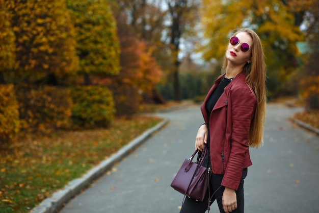 Donna bionda glamour con labbra rosse che indossa giacca di pelle, borsa e occhiali rossi. Spazio per il testo