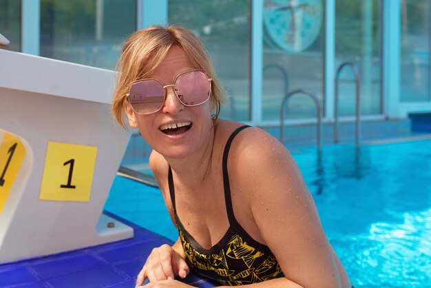 donna bionda in costume da bagno e occhiali da sole rosa a bordo piscina estate