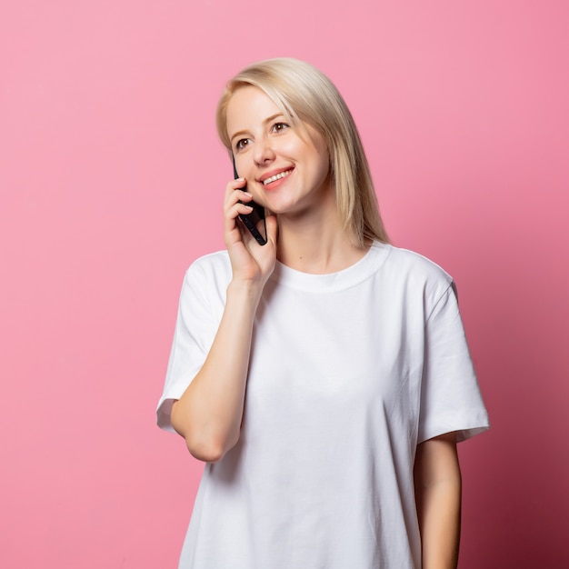 Donna bionda in maglietta bianca con il cellulare in rosa