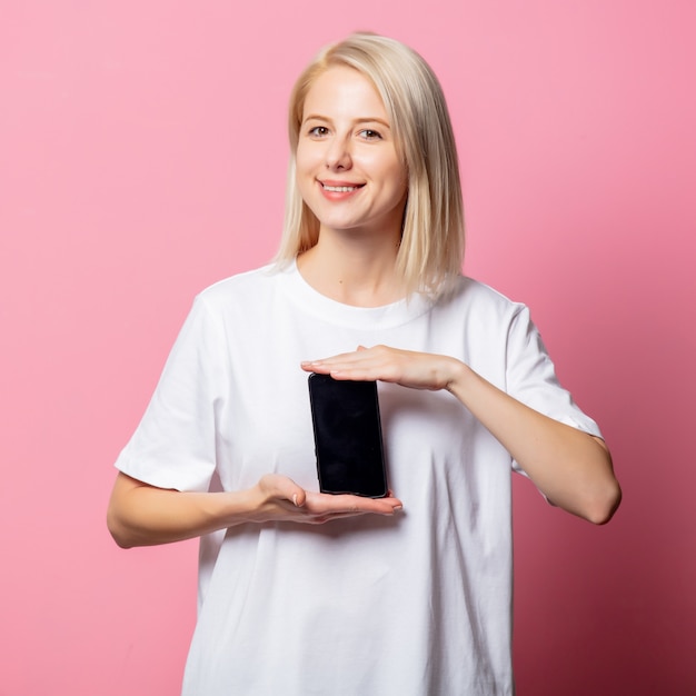 Donna bionda in maglietta bianca con il cellulare in rosa