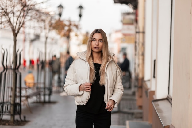 donna bionda in una giacca bianca in abito nero è in posa in città