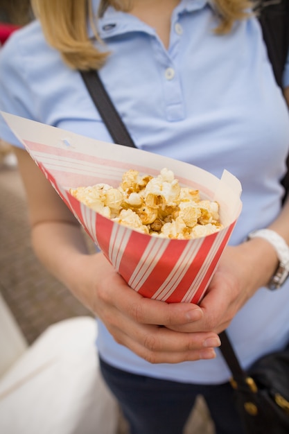 Donna bionda in una maglietta blu con un sacchetto di carta a righe pieno di popcorn