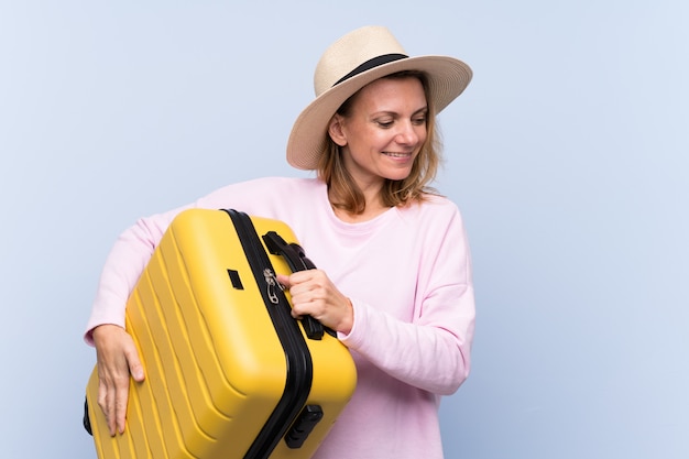 Donna bionda in vacanza con la valigia da viaggio e un cappello