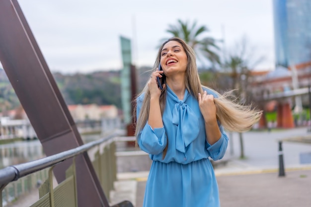 Donna bionda in vestito blu che sorride parlando al telefono al fiume nel concetto di stile di vita della città