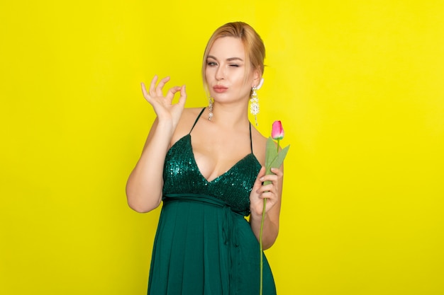 Donna bionda in vestito verde che tiene un tulipano rosa