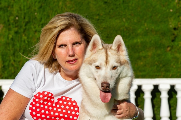 Donna bionda matura seduta sull'erba con il cane husky siberiano vicino alla piscina