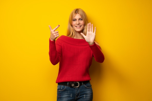 Donna bionda oltre muro giallo contando sette con le dita