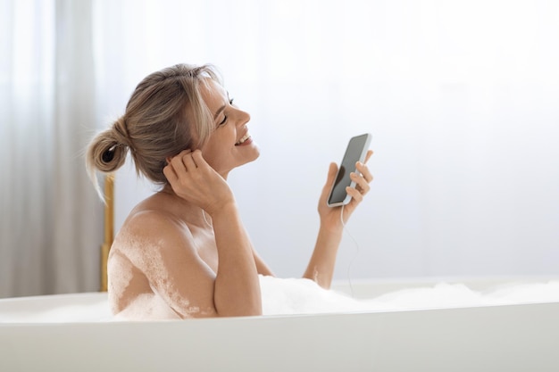 Donna bionda positiva che fa un bagno schiumoso e ascolta musica