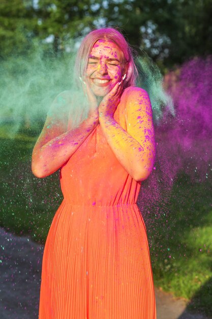 Donna bionda positiva con capelli lunghi che posano con l'esplosione di vernice Holi viola e verde