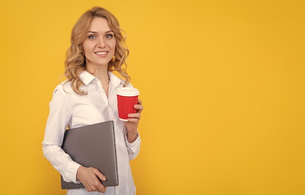 Donna bionda positiva con tazza di caffè e laptop su sfondo giallo