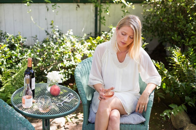 Donna bionda seduta in un giardino in estate con in mano un bicchiere di vino